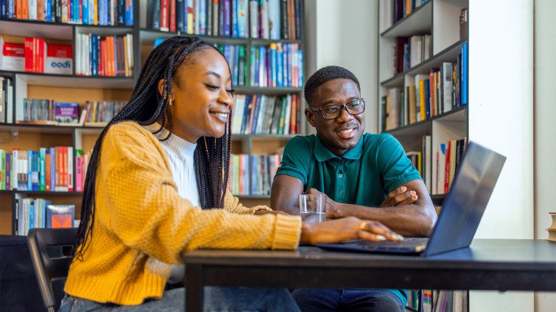 Two HBCU students working together on a laptop in a library