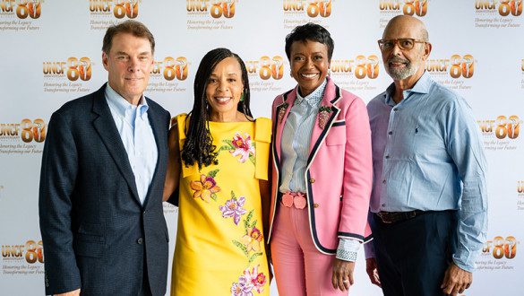 Four people standing in front of a UNCF 80th anniversary banner