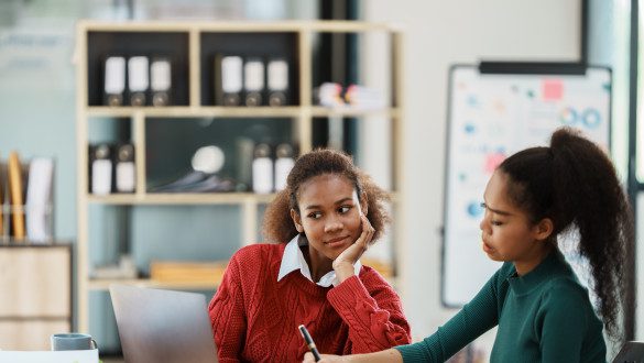 Focused young african american businesswoman or student looking at laptop holding book learning, serious black woman working or studying with computer doing research or preparing for exam online