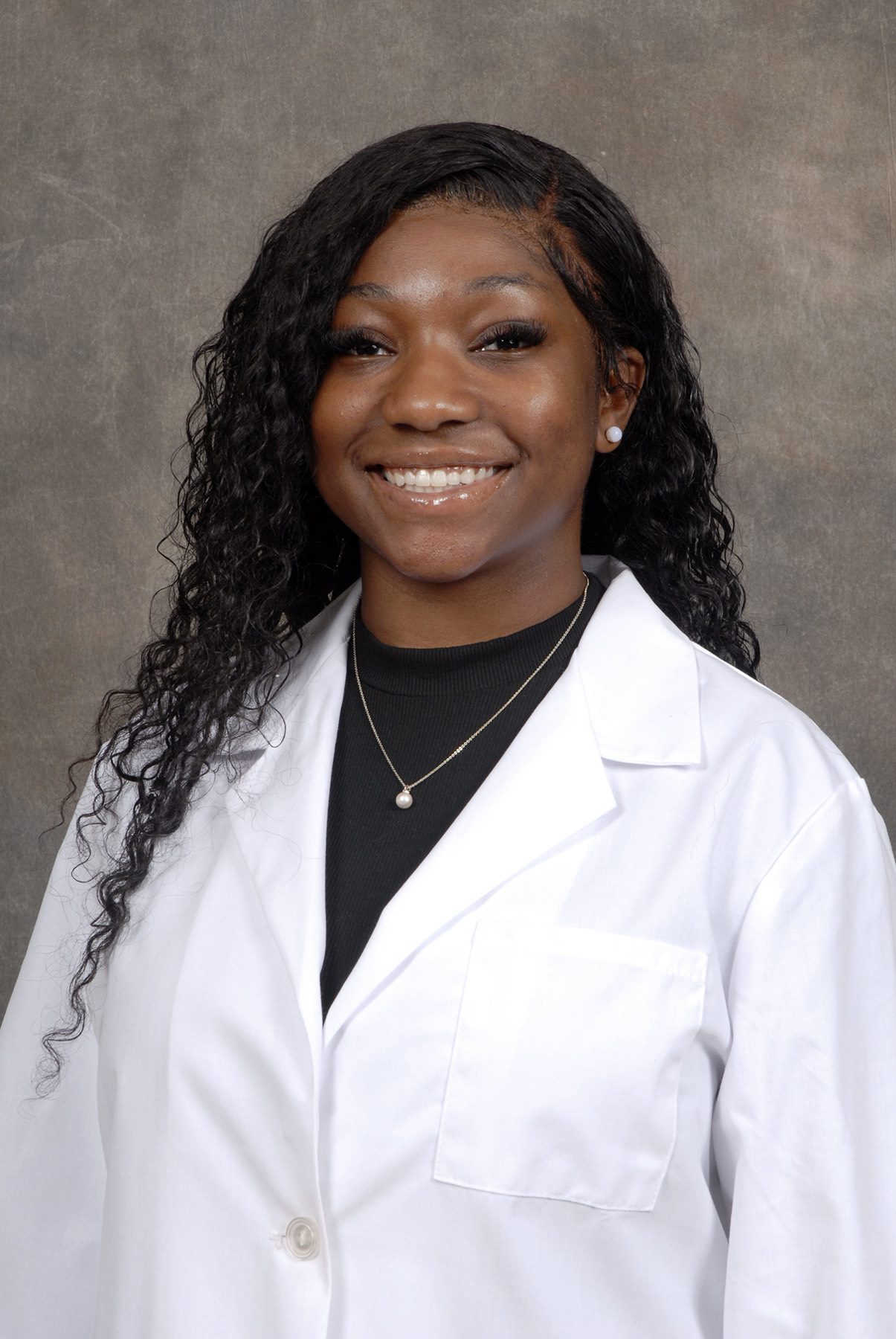Aniya Diggs in front of a gray background wearing a white doctor's coat and black shirt.