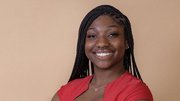 Aniya Diggs, a recent graduate of Xavier University of Louisiana, a UNCF-member institution, smiling wearing a red shirt in front of a brown background.
