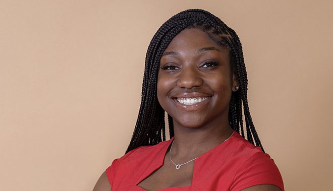 Aniya Diggs, a recent graduate of Xavier University of Louisiana, a UNCF-member institution, smiling wearing a red shirt in front of a brown background.