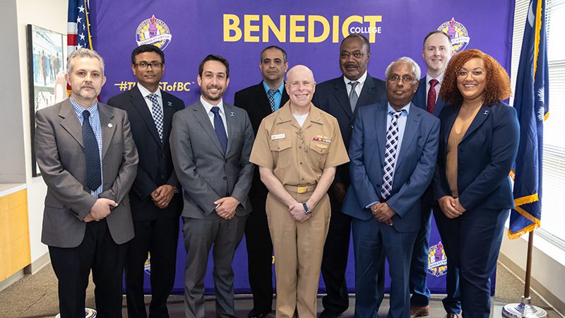 Six people standing in front of a Benedict college banner