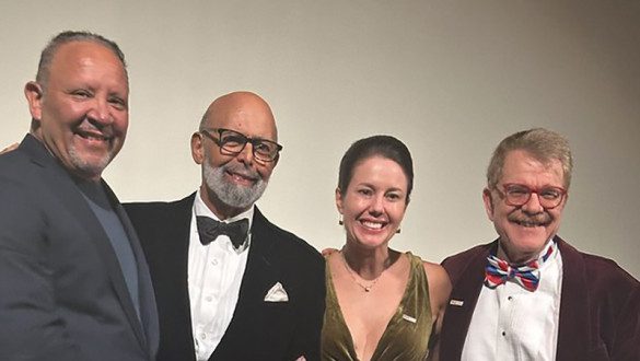 Dr. Michael Lomax wears a tuxedo and black bowtie, holds a glass award and smiles.