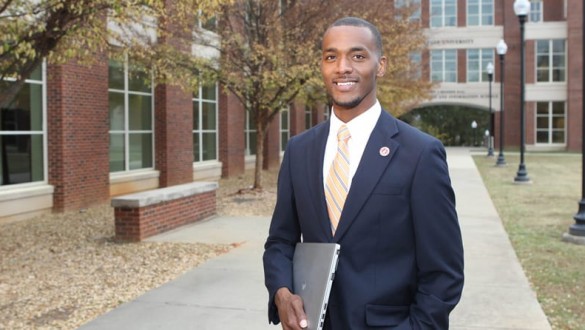 Male college student with laptop wearing a suit outside on college campus