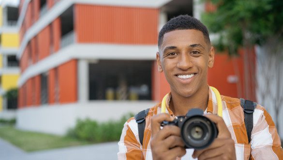 Portrait of professional African American photographer taking pictures on the street looking at camera. Tourist holding digital camera outdoors, copy space. Travel concept