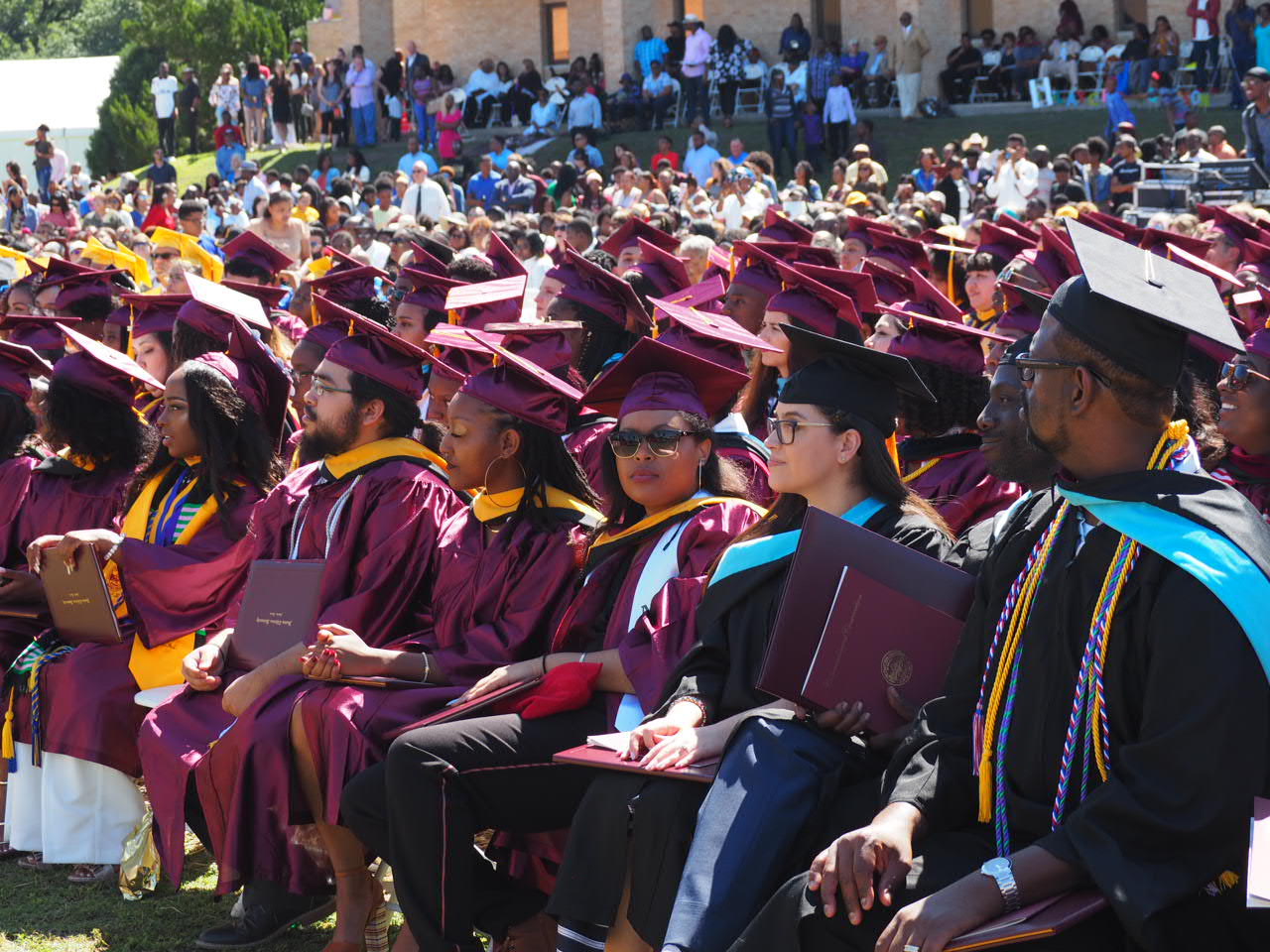 A group of students wearing caps and gowns sit at a graduation ceremony