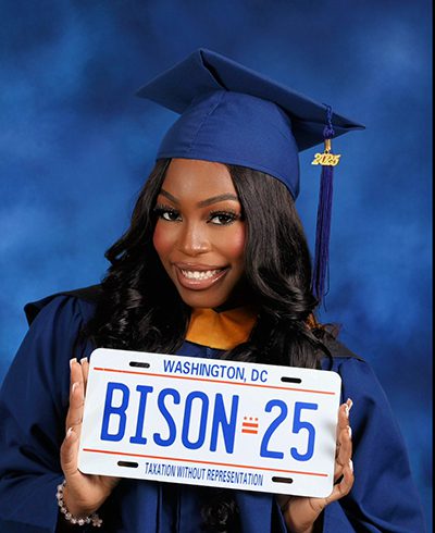Lenah Alghali in a blue graduation gown and hat with a blue tassel that has 2025 in gold. She holds a Washington, D.C. license plate that says Bison 25 on it and Taxation Without Representation and has the Washington, D.C. flag symbol, three red stars on top and two red bars underneath them.