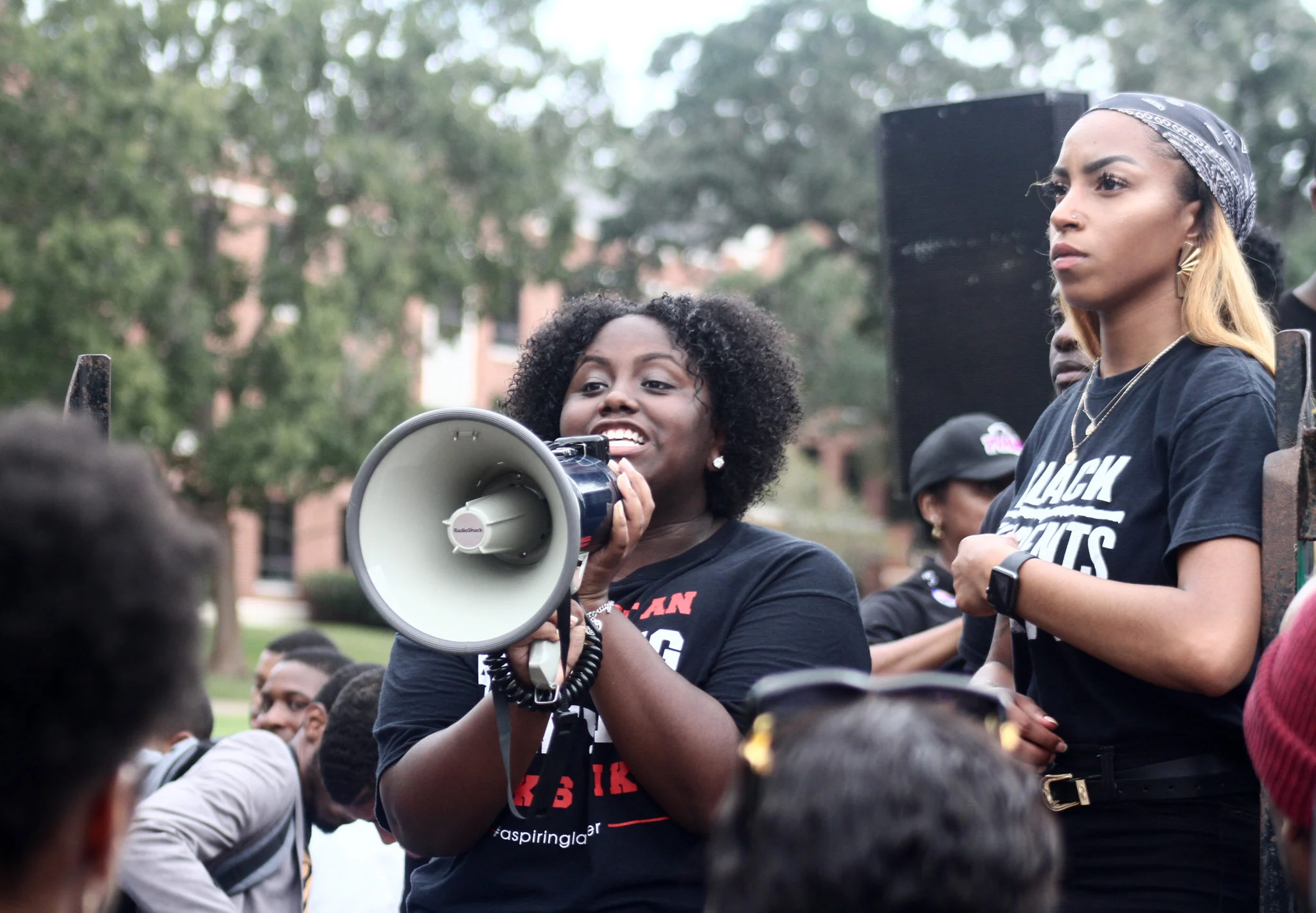A woman stands with a megaphone in a large crowd at a rally.