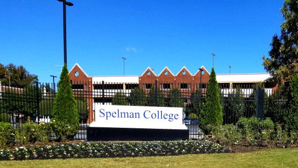Spelman College is a historically Black college in Atlanta, GA. A campus building in the background, a sign spelling out Spelman College in blue in the foreground with landscaping surrounding it.