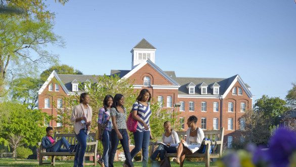 Spelman College is a historically Black college in Atlanta, GA. Students walk past a campus building in the background and greenery and flowers in the foreground.