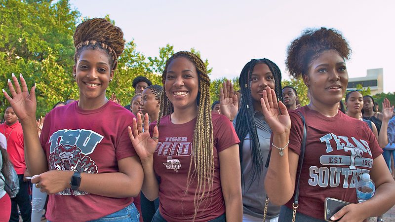 A group of students wearing TSU shirts stand with their right hands raised