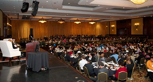Conference room with large number of people seated watching discussion take place