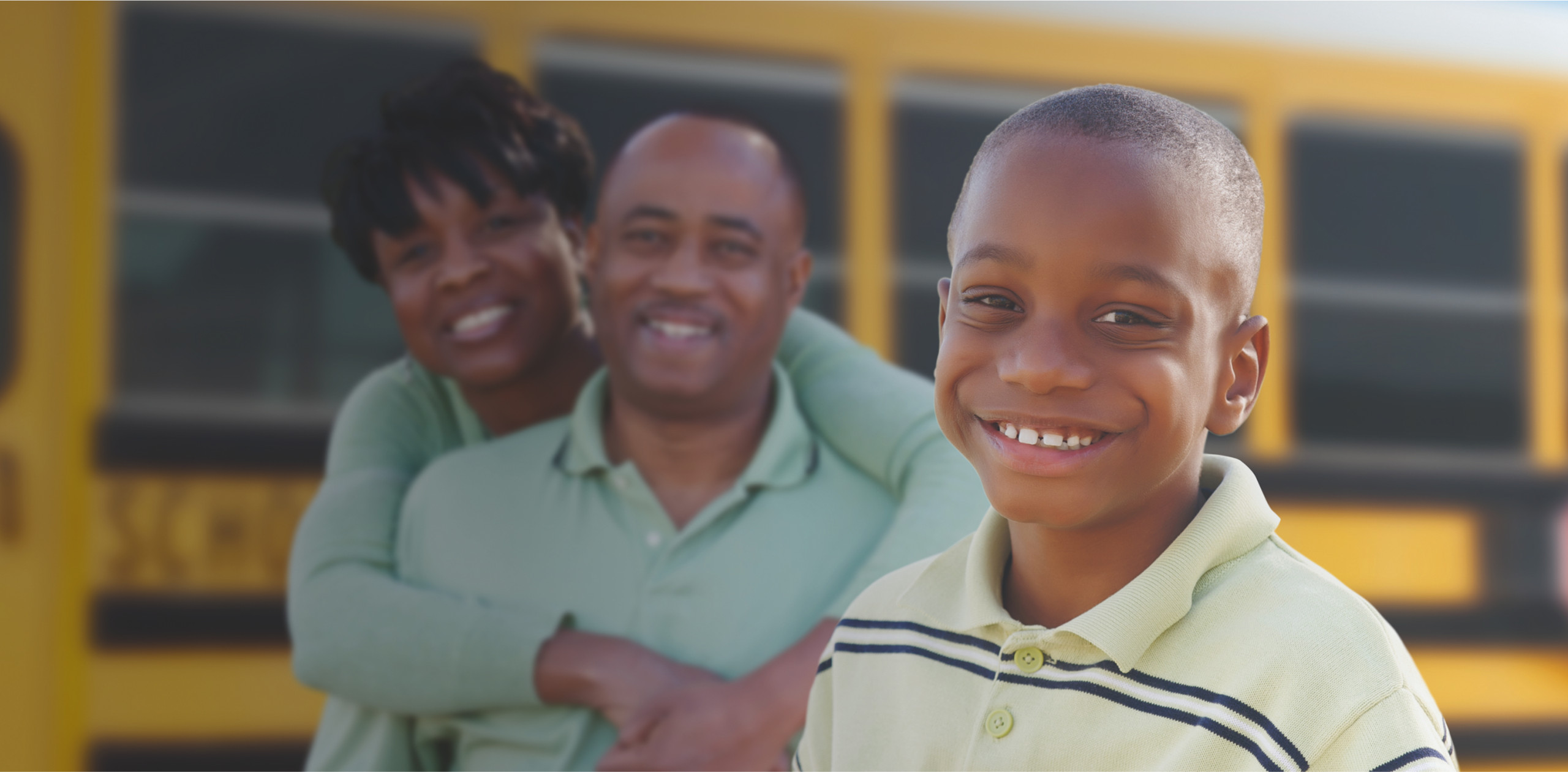 Boy Smiling with Parents and Yellow school bus in background